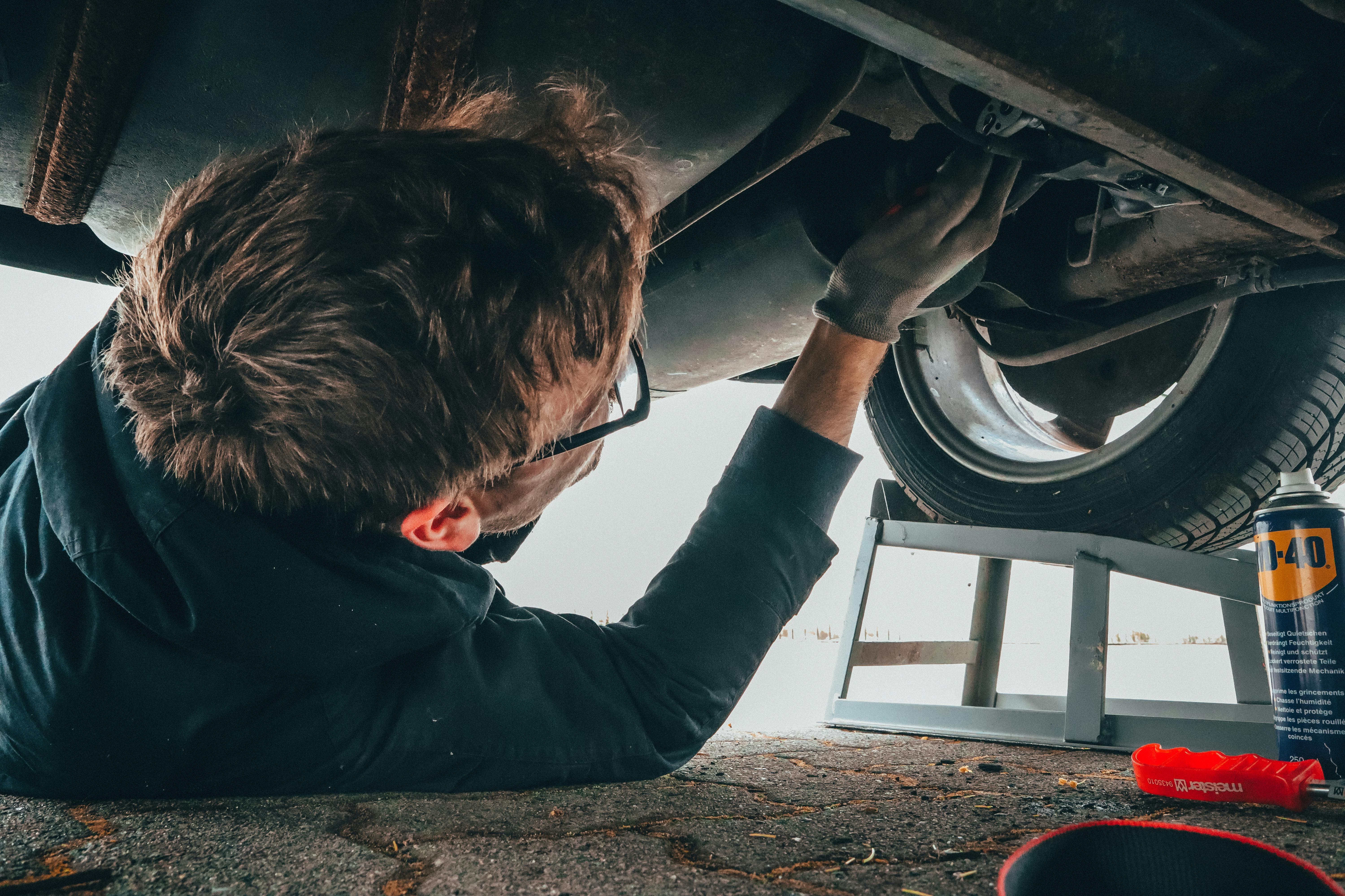 A image of a man looking underneath a car