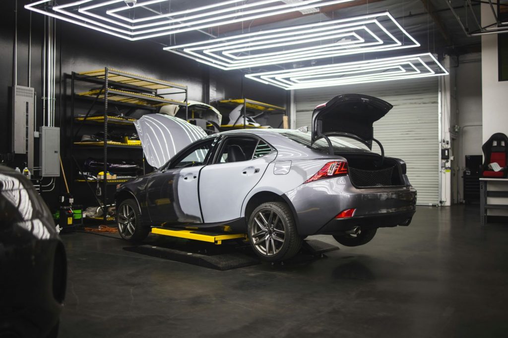 Car in a garage undergoing MOT inspection, with hood and trunk open