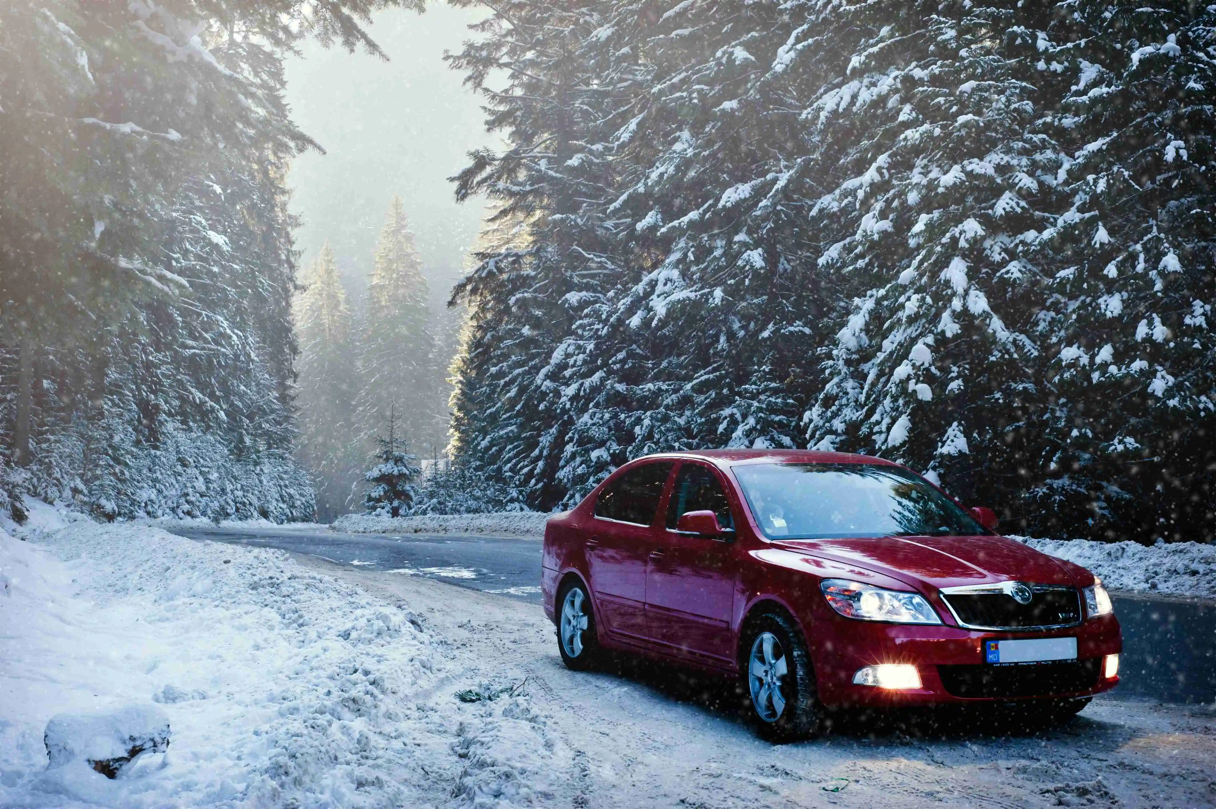 A red car driving on a snowy road, highlighting the need for proper winter car maintenance.
