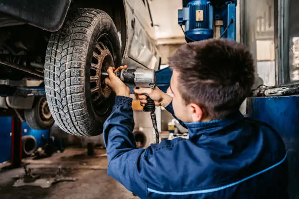 worker screwing bolts on the car wheel.