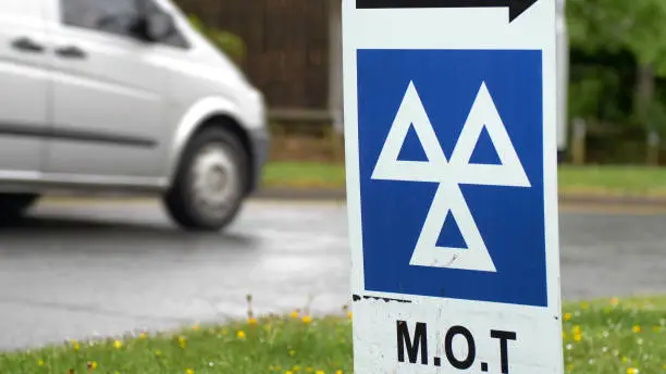 car driving into automotive workshop passing a MOT sign.