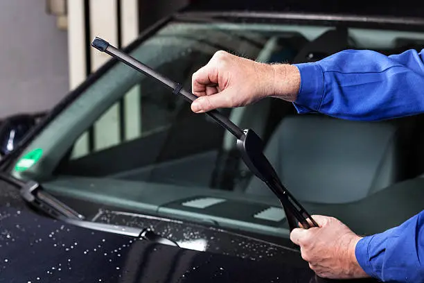 worker installing wiper blades on a car.